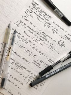 three pens sitting on top of a piece of paper next to some writing utensils