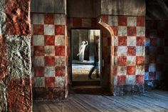 a person standing in front of a mirror on top of a wooden floor with red and white checkered walls