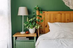 a bed with a wooden headboard and green walls next to a nightstand with a potted plant on it