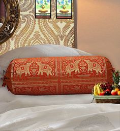 an orange pillow sitting on top of a bed next to a bowl of fruit and a mirror