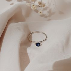 a ring with a blue stone sits on a white cloth next to some small flowers