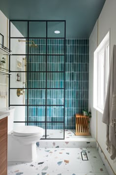 a bathroom with blue tiled walls and flooring next to a white toilet in front of a window