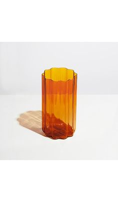 an orange glass vase sitting on top of a white table next to a brown object