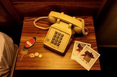 an old style phone sitting on top of a wooden table next to coins and cards