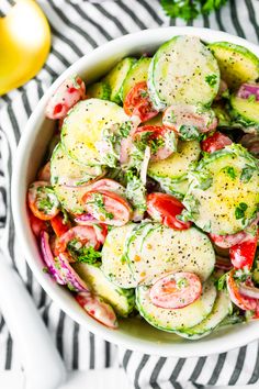 a white bowl filled with cucumber salad and topped with tomatoes, onions, red onion, lettuce and parsley