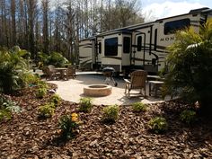 an rv is parked in the woods next to a fire pit and table with chairs