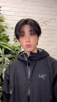 a young man standing in front of a brick wall wearing a black jacket with an embroidered dragon on it