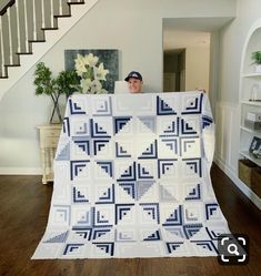 a man holding up a quilt in front of a stair case with stairs behind him