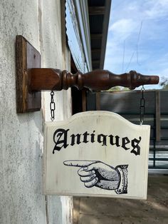 a wooden sign hanging from the side of a building with a hand pointing at it