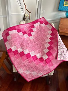 a pink and white quilt sitting on top of a chair next to a stair case