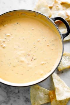 a pot filled with cheese dip surrounded by tortilla chips on a marble surface