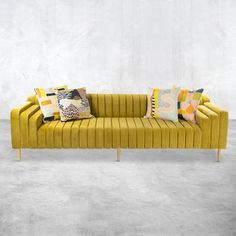 a yellow couch with colorful pillows on it in front of a white wall and concrete floor