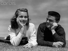 a man and woman laying on the grass with their hands to their face, smiling