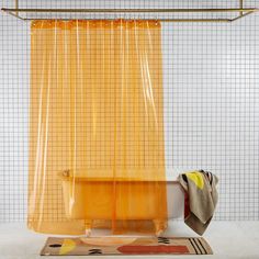 a yellow shower curtain hanging over a bathtub next to a rug and towel rack