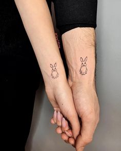 two people holding hands with small tattoos on their wrist and one has a rabbit tattoo on it