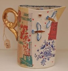 a ceramic pitcher with birds and flowers painted on the side, next to a pair of scissors