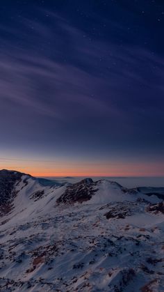 the night sky is lit up over a snowy mountain range with stars in the distance