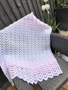 a white and pink crocheted blanket sitting on top of a wicker chair