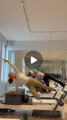 two women are doing exercises on treadmills in a room with large windows and lots of exercise equipment