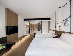 two beds in a room with white linens and wood flooring next to a flat screen tv