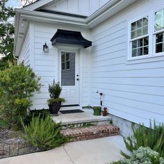 a white house with a black door and some plants on the front steps in front of it