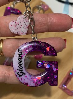 someone is holding up the letter g with glitter on it and heart shaped keychains