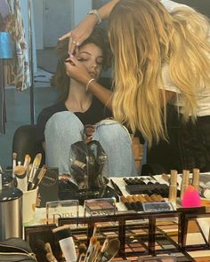 two women sitting in front of a table full of makeup and other cosmetics on display