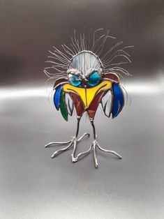 a colorful bird made out of glass sitting on top of a metal surface with its legs spread