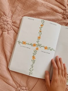 a person is holding an open book on a bed with pink sheets and orange flowers