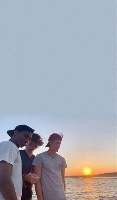 three young men standing next to each other in front of the ocean at sunset or sunrise