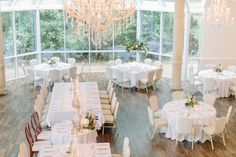 a room filled with tables and chairs covered in white tablecloths, chandeliers and flowers