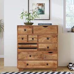 a wooden dresser with drawers in a white room next to a potted plant on top of it