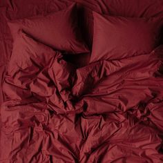 an unmade bed with red sheets and pillows