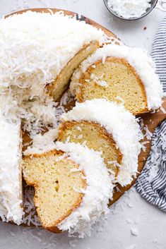 a cake with white frosting and coconut toppings on a wooden platter next to two small bowls