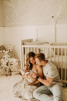 a man and woman are sitting on the floor next to a crib with a baby in it