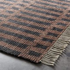 a brown and black rug with fringes on the bottom, in front of a gray wall