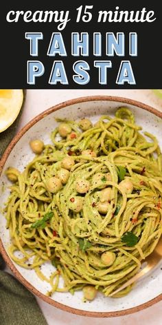 a bowl filled with pasta and garnished with pesto on top, next to lemon wedges