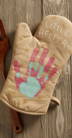 a little helper oven mitt sitting on top of a wooden table next to a spatula