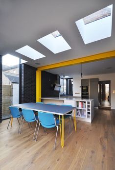 a dining room table with blue chairs in front of an open kitchen and skylights