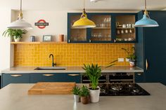 a kitchen with yellow and blue cabinets, potted plants on the counter top and hanging lights above it