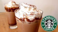 two glasses filled with hot chocolate and whipped cream on top of a wooden table next to a starbucks logo