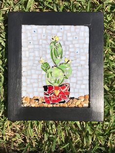 there is a small glass mosaic with a cactus in it on the grass and rocks