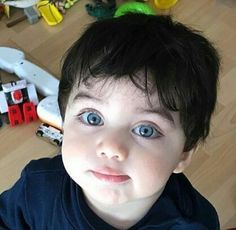 a young boy with blue eyes looking up at the camera while standing in front of toys