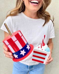 a woman holding a cupcake with an american flag hat on it and a straw in her hand