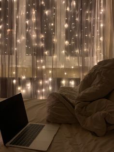 a laptop computer sitting on top of a bed next to a window covered in lights