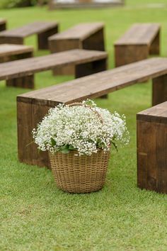 a basket filled with flowers sitting on top of a grass covered field next to wooden benches