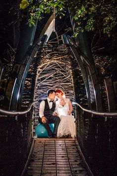 a bride and groom are sitting on a bridge at night in their wedding photo shoot