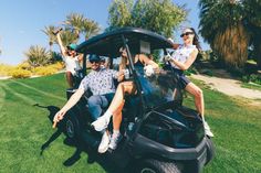 three people sitting on the back of a golf cart with their arms in the air