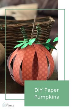 an orange paper pumpkin sitting on top of a table next to a basket with green leaves