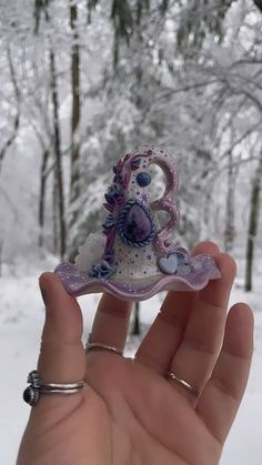 a hand holding a small glass figurine in front of snow - covered trees